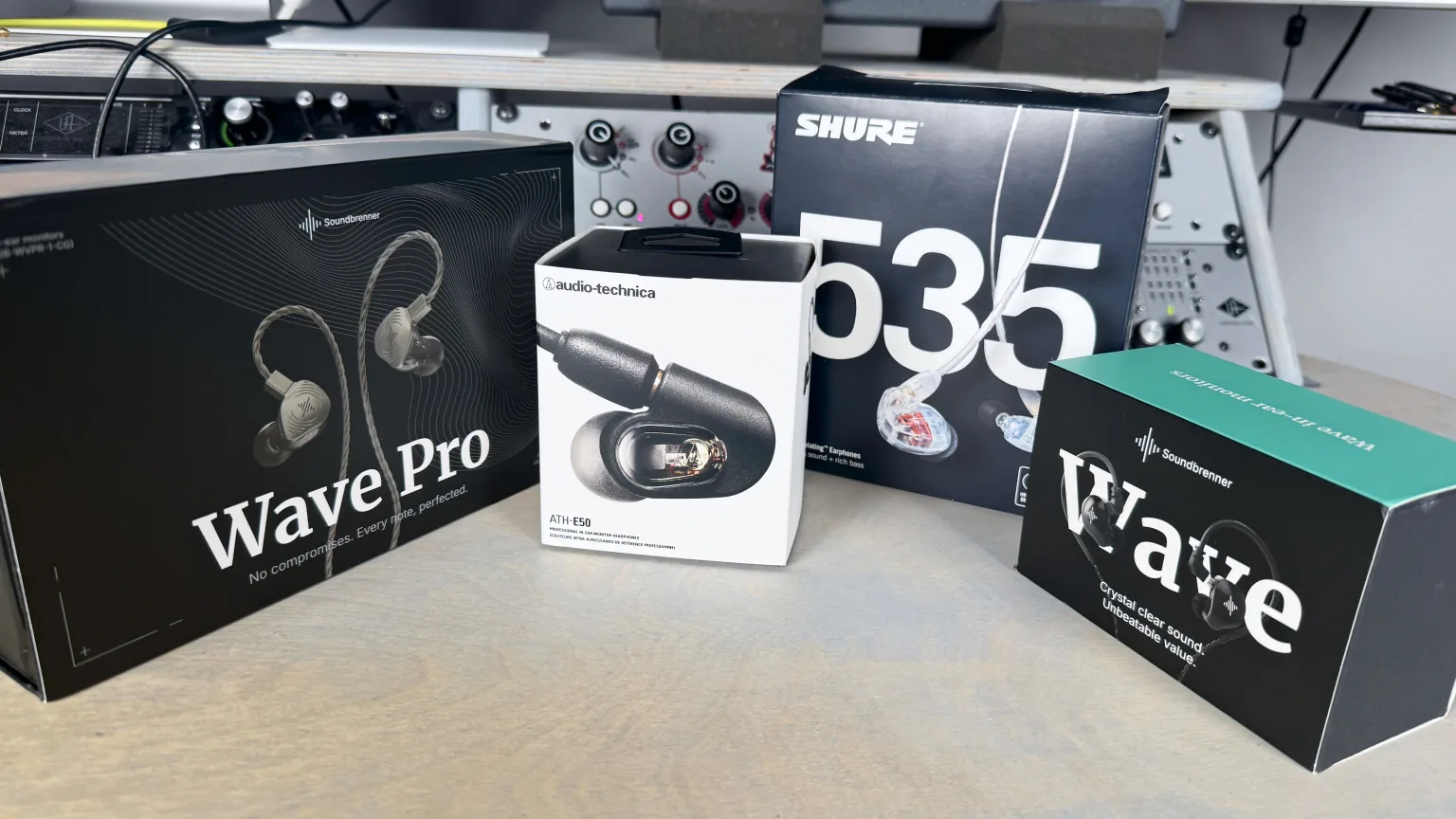 Retail boxes of the Soundbrenner Wave Pro 2, Audio-Technica ATH-E50, Shure SE535, and Soundbrenner Wave on the studio desk