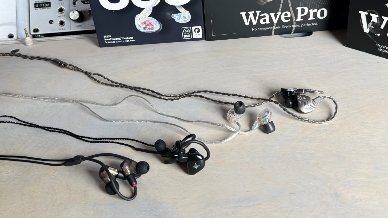 Four unboxed in-ear monitors with cables laid out on the studio desk in front of their packaging